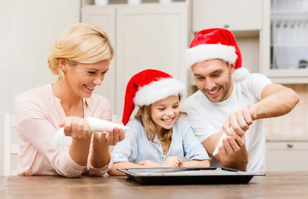 Happy family in santa helper hats making cookies — Stock Photo, Image