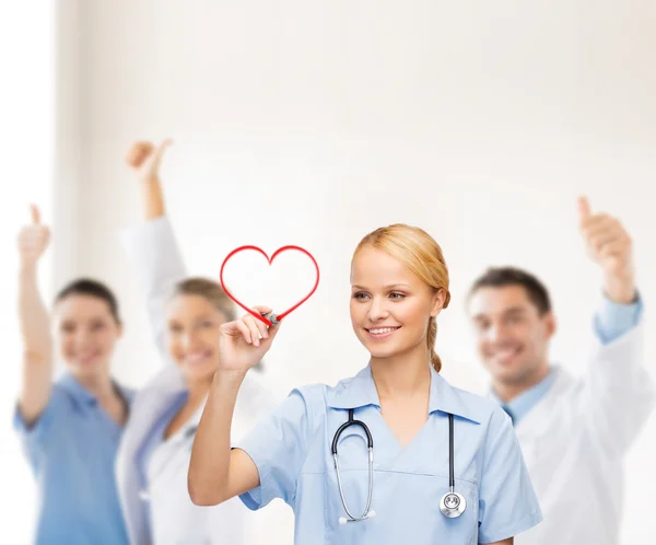 Médico sonriente o enfermera dibujando corazón rojo — Foto de Stock