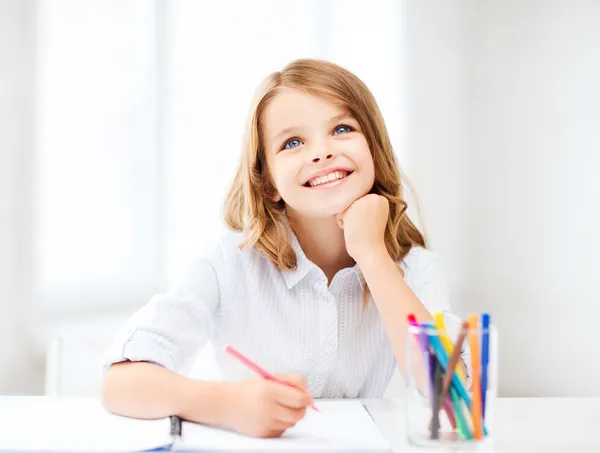 Улыбающаяся маленькая студентка рисует в школе — стоковое фото