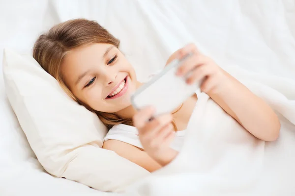 Kleines Mädchen mit Smartphone spielt im Bett — Stockfoto