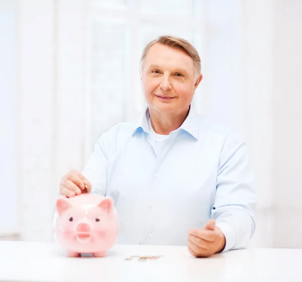 Velho colocando moeda em grande banco porquinho — Fotografia de Stock