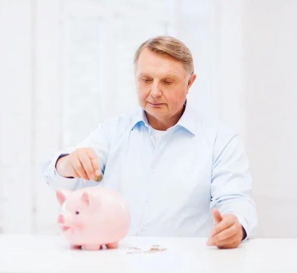 Alter Mann steckt Münze in großes Sparschwein — Stockfoto