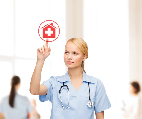 Улыбающийся доктор или медсестра, указывающие на икону больницы — стоковое фото