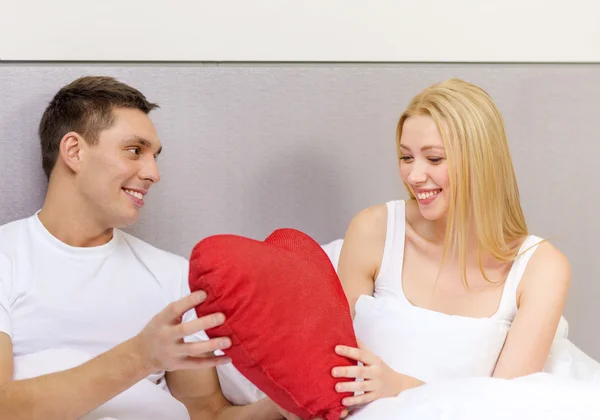 Smiling couple in bed with red heart shape pillow — Stock Photo, Image