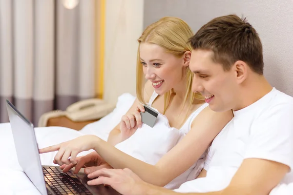 Casal na cama com computador portátil e cartão de crédito — Fotografia de Stock