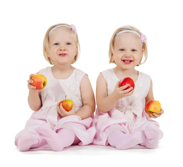 Две одинаковые девочки-близнецы играют с яблоками — стоковое фото