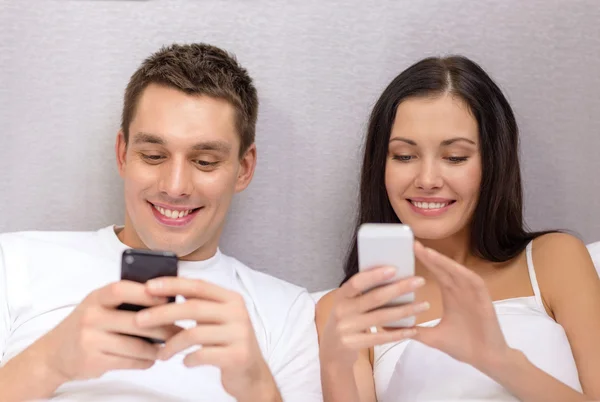 Lächelndes Paar im Bett mit Smartphones — Stockfoto