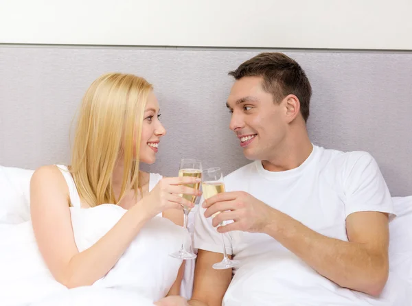 Pareja sonriente con copas de champán en la cama — Foto de Stock