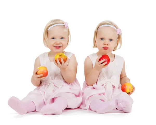 Twee identieke tweeling meisjes spelen met appels — Stockfoto