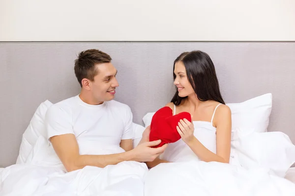Çift yatakta kırmızı kalp şekli yastık ile gülümseyen — Stok fotoğraf