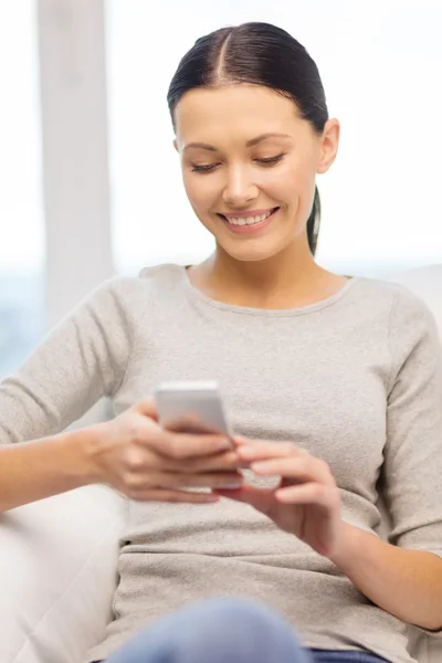 Mulher sorridente com smartphone em casa — Fotografia de Stock