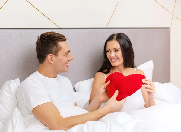 赤いハート形の枕とベッドでカップルの笑みを浮かべてください。 — ストック写真