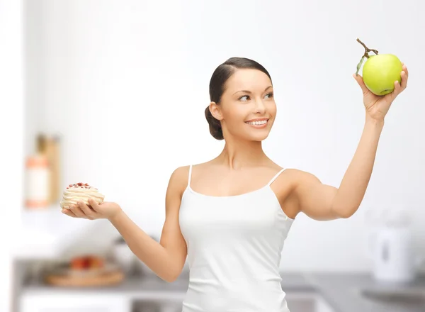 Sporty woman with apple and cake in kitchen — Stock Photo, Image