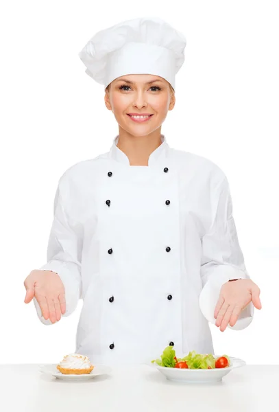 Chef feminino sorridente com salada e bolo em pratos — Fotografia de Stock