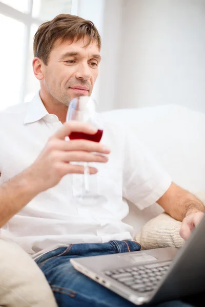 Hombre con ordenador portátil y copa de vino tinto — Foto de Stock