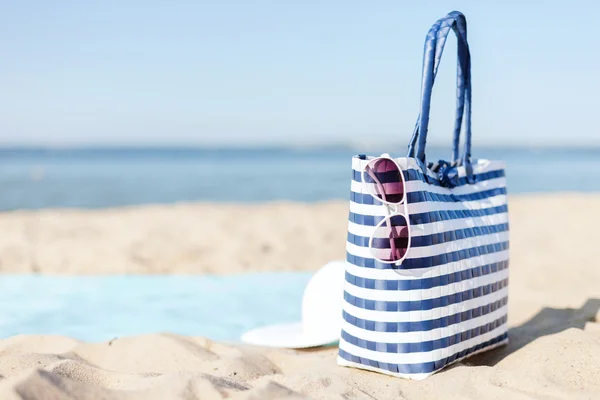 Strohhut, Sonnenbrille und Tasche liegen im Sand — Stockfoto