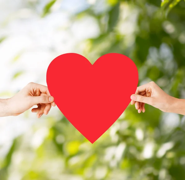 Mãos de casal segurando coração vermelho — Fotografia de Stock