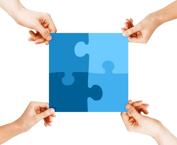 Four hands connecting puzzle pieces — Stock Photo, Image