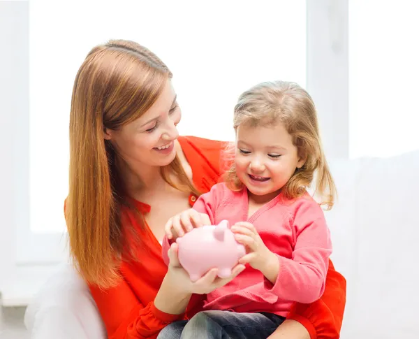 Happy mother and daughter with small piggy bank — Stock Photo, Image