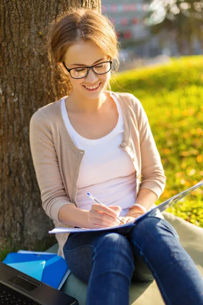 Lachende tiener in brillen schrijven in notitieblok — Stockfoto