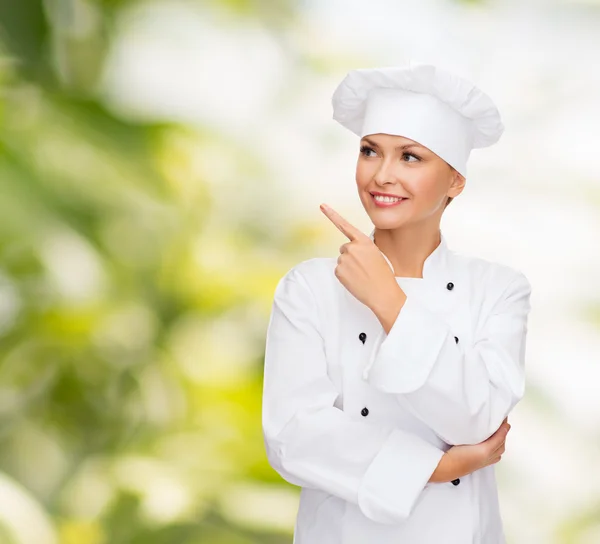 Uśmiechnięta kobieta kucharz palcem wskazującym na sonething — Zdjęcie stockowe