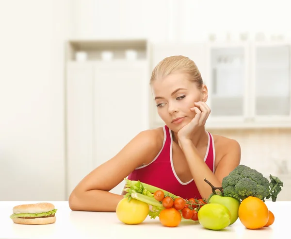 Pochybující žena s ovocem a hamburger — Stock fotografie