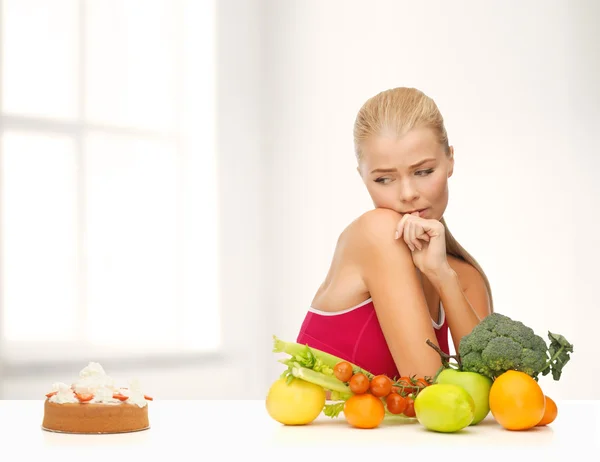 Mulher duvidando com frutas e torta — Fotografia de Stock