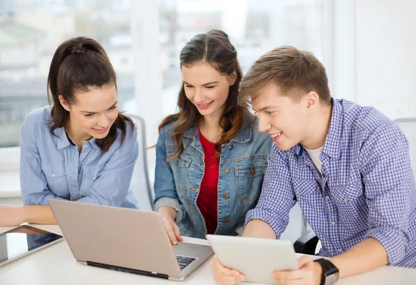Tres estudiantes sonrientes con ordenador portátil y tableta PC —  Fotos de Stock