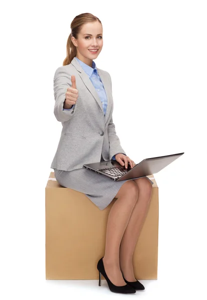 Mulher sorridente sentada em caixa de papelão com laptop — Fotografia de Stock