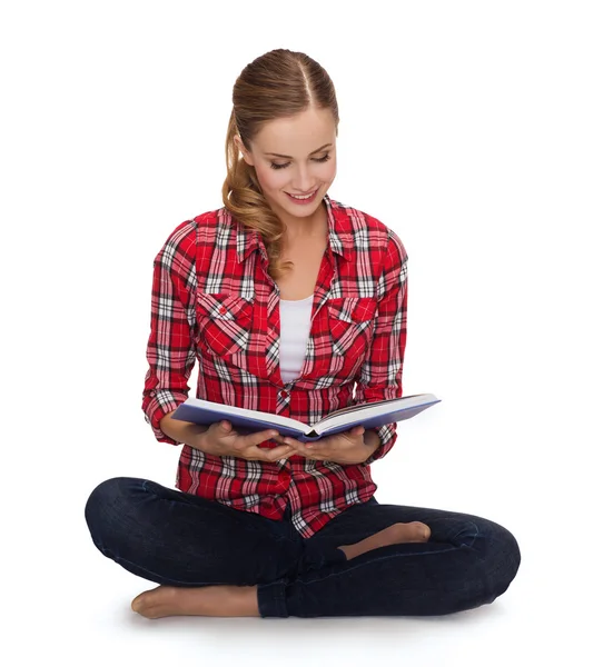 Smiling young woman sittin on floor with book — Stock Photo, Image