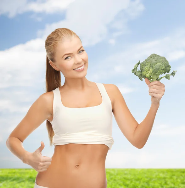 Vrouw wijzend op haar abs en houden van broccoli — Stockfoto