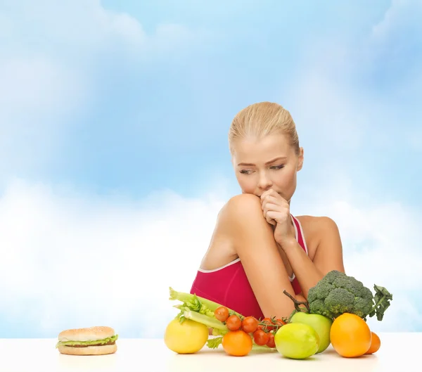 Mulher duvidando com frutas e hambúrguer — Fotografia de Stock