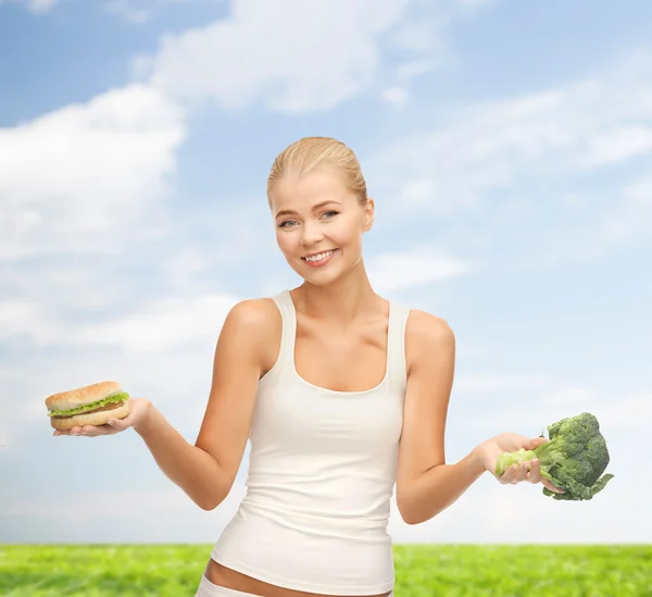 Leende kvinna med broccoli och hamburgare — Stockfoto