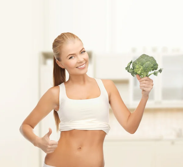 Mujer señalando sus abdominales y sosteniendo brócoli —  Fotos de Stock