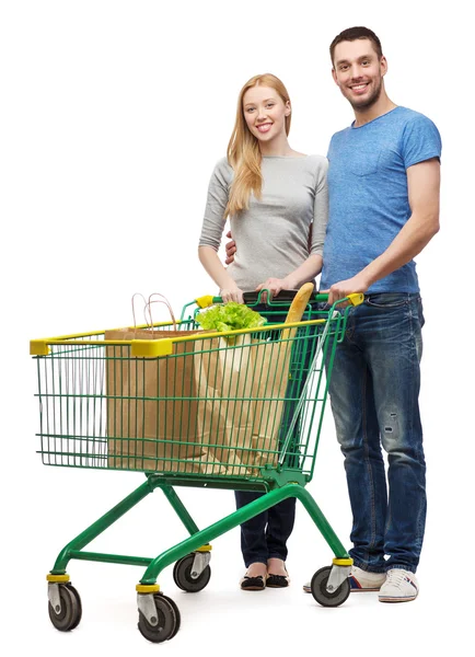 Uśmiechający się para z koszyka na zakupy i jedzenie w nim — Zdjęcie stockowe