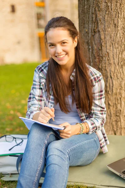 Lachende tiener schrijven in notitieblok — Stockfoto