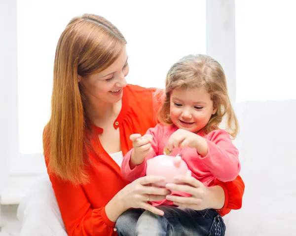 Mãe feliz e filha com pequeno banco porquinho — Fotografia de Stock