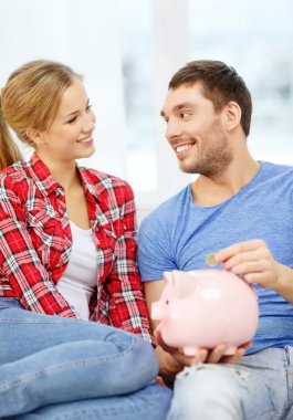 Smiling couple with piggybank sitting on sofa clipart
