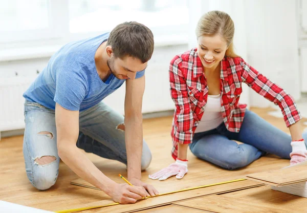 Coppia sorridente misurazione pavimenti in legno — Foto Stock