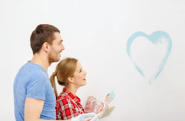 Smiling couple painting small heart on wall — Stock Photo, Image