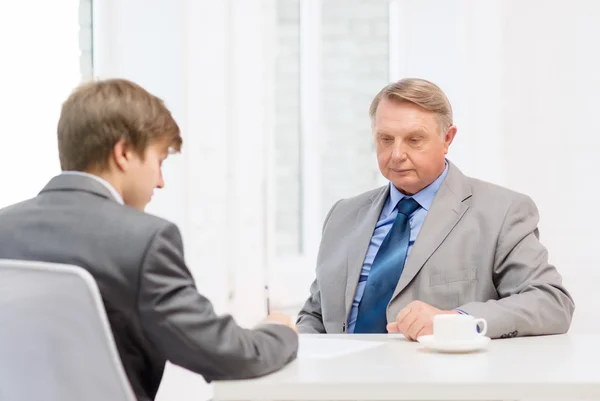 Older man and young man signing papers in office — Stock Photo, Image