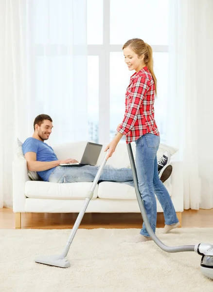 Mujer sonriente con aspiradora y hombre con portátil — Foto de Stock