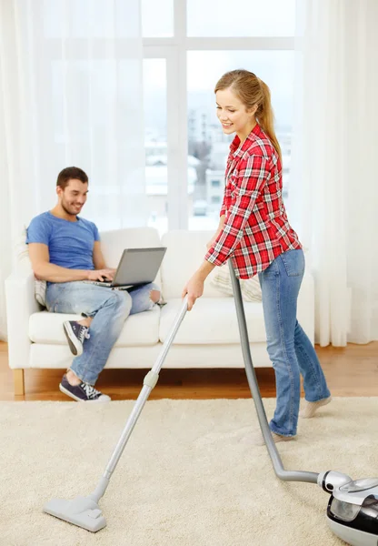 Smiling woman with hoover and man with laptop — Stock Photo, Image