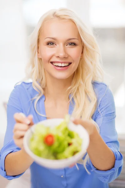 Lachende jonge vrouw met groene salade thuis — Stockfoto