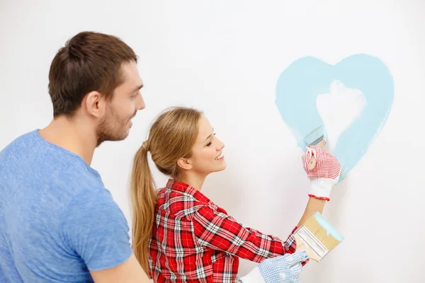 Smiling couple painting small heart on wall — Stock Photo, Image