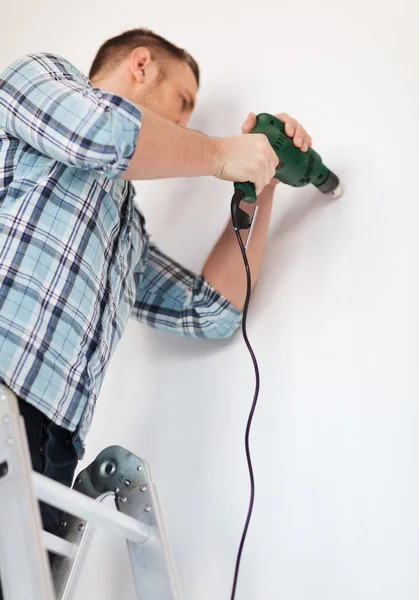 Человек с электрическим сверлом делает отверстие в стене — стоковое фото