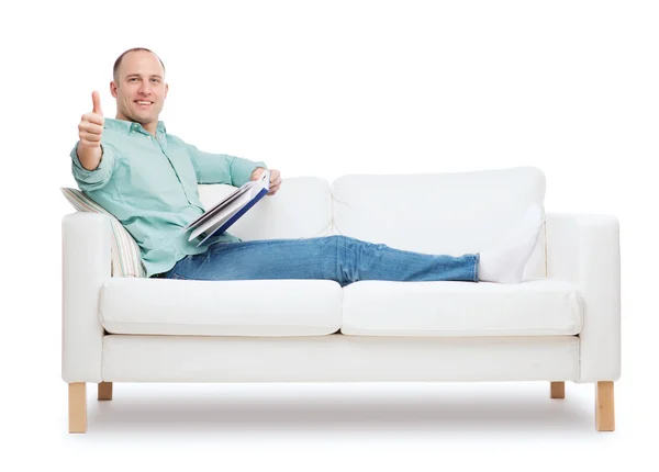 Uomo sorridente sdraiato sul divano con libro — Foto Stock