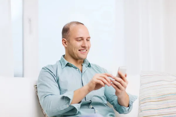 Uomo sorridente con smartphone a casa — Foto Stock