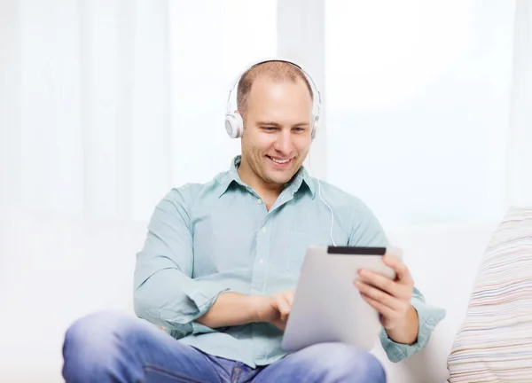 Uomo sorridente con tablet pc e cuffie a casa — Foto Stock