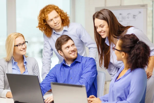 Equipo sonriente con computadoras portátiles en la oficina —  Fotos de Stock